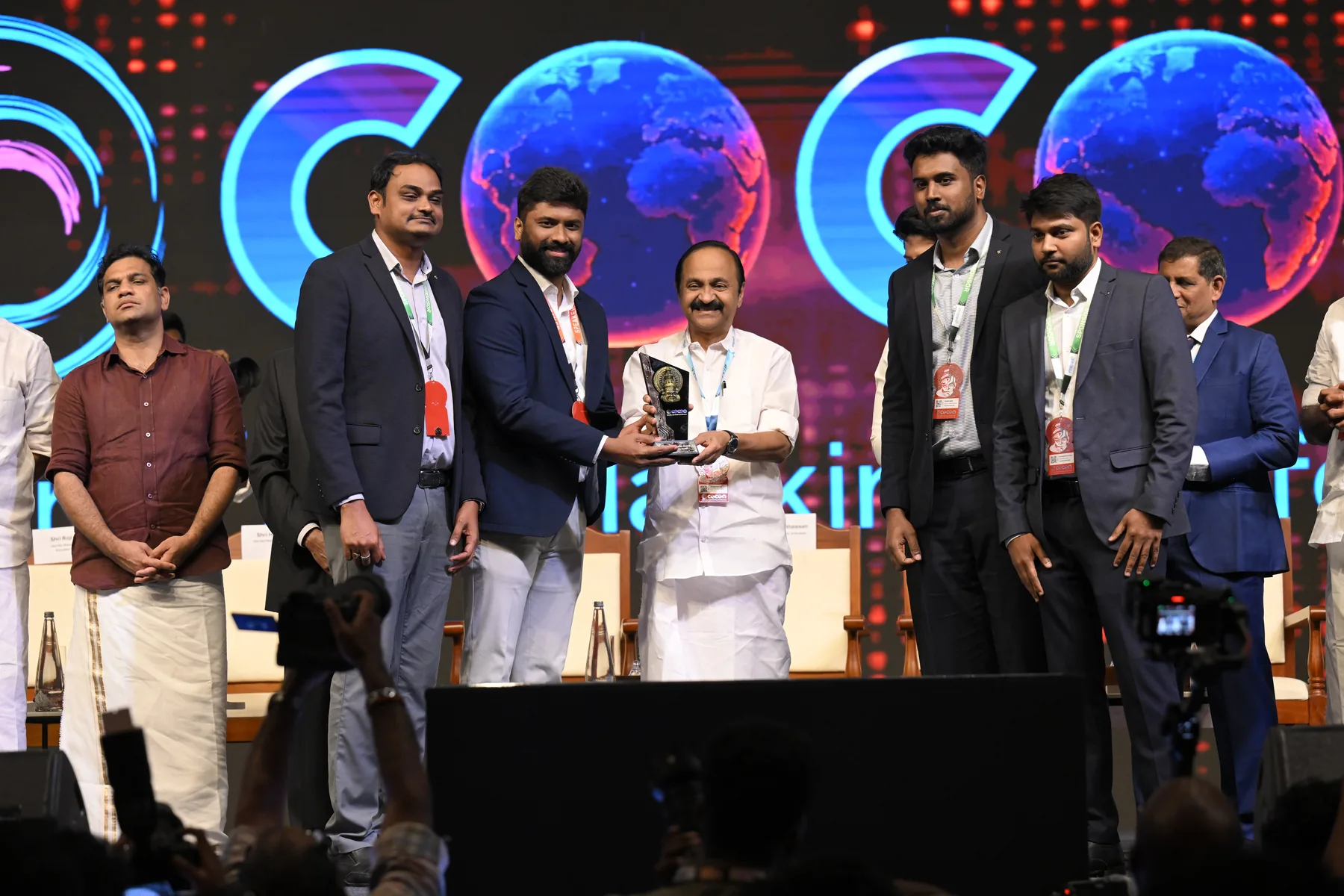 Members of the Spharaka Networks team on stage at C0C0N 2026, receiving a memento from the Hon'ble Chief Minister of Kerala in front of the conference's globe backdrop.